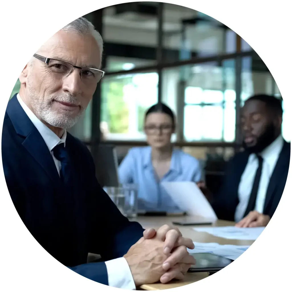 Three business professionals in a meeting, with a senior executive in the foreground looking at the camera